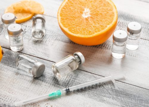 Vials and a syringe next to a sliced orange