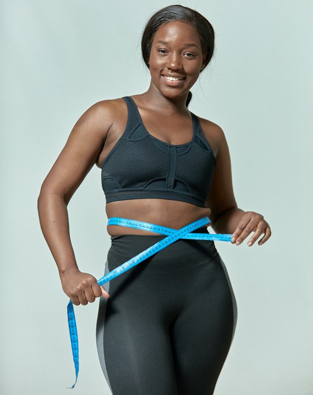 Smiling woman measuring her waistline with a tape measure